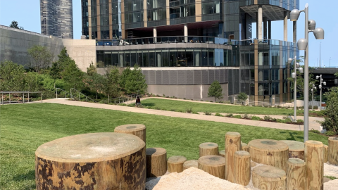 A sloping park next to a high-rise and elevated roadway. 